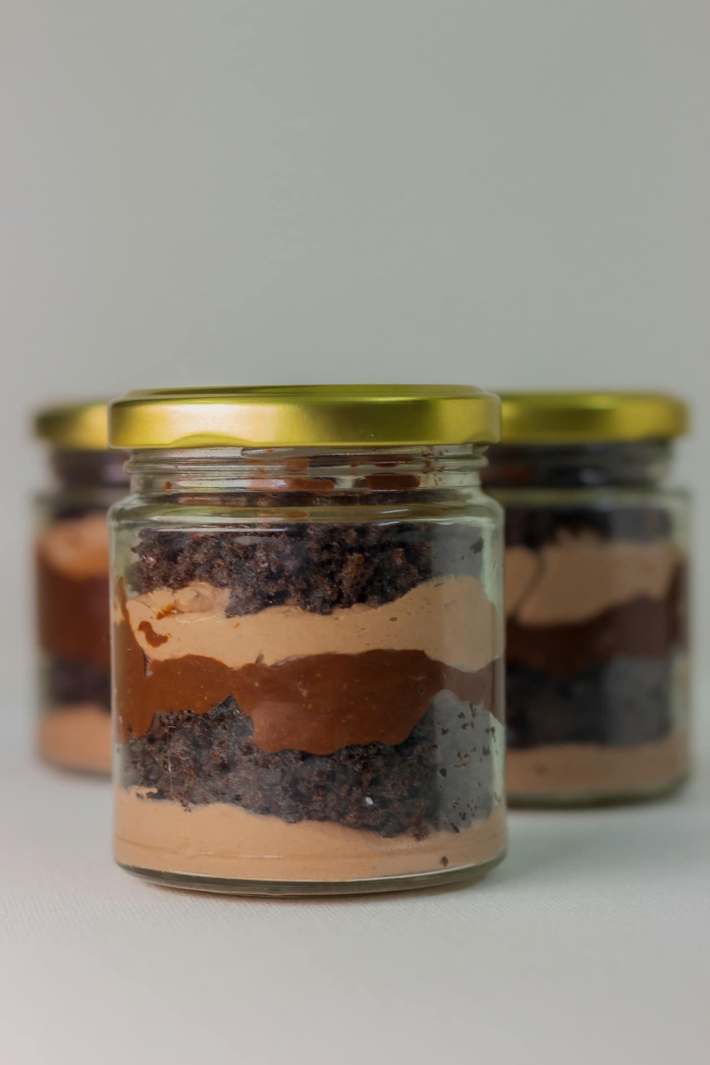 Layers of chocolate cake and cream in a glass cup with a gold lid