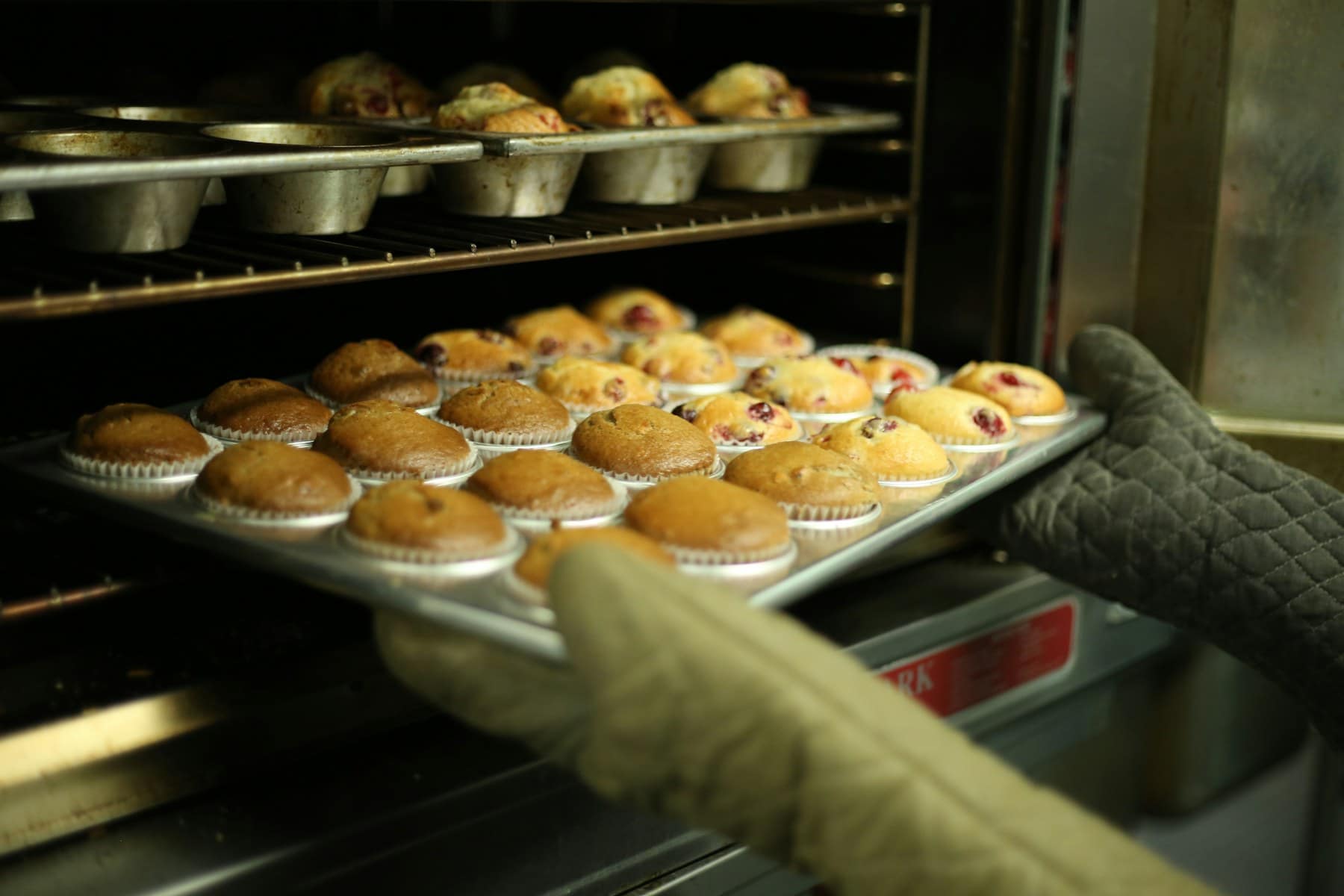 A tray of golden muffins being lifted out of a home oven with an oven glove