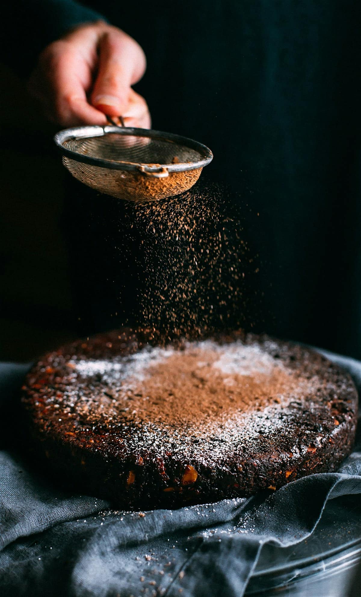 Cocoa powder falling through a sieve onto a dark chocolate cake