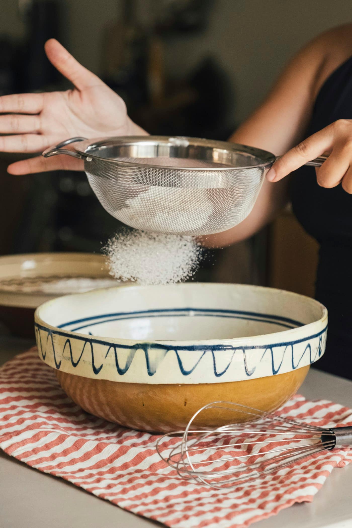 Hands sifting flour into a hand-painted ceramic bowl